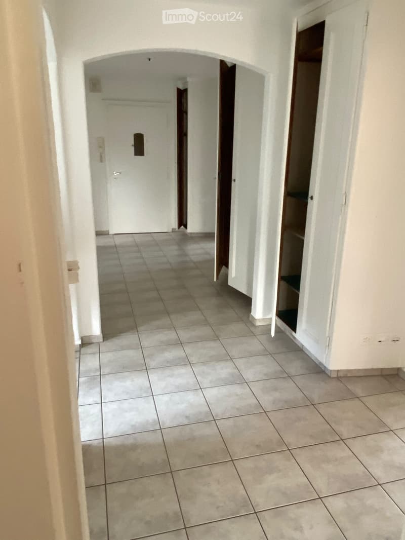 Empty hallway with tiled floor, white walls, and open doors leading to other rooms.