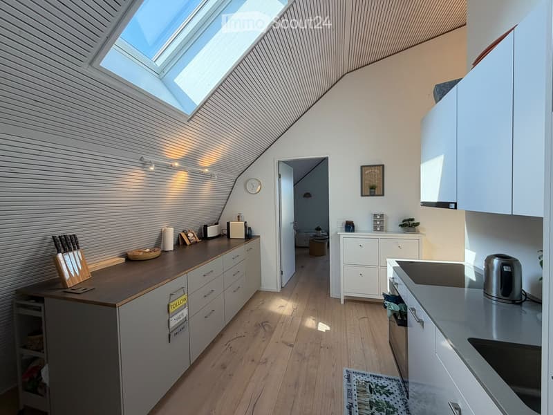Modern kitchen with white cabinets, wooden countertops, and a skylight above. Includes a knife block, toaster, small plant, and a small table with a bowl and cup.