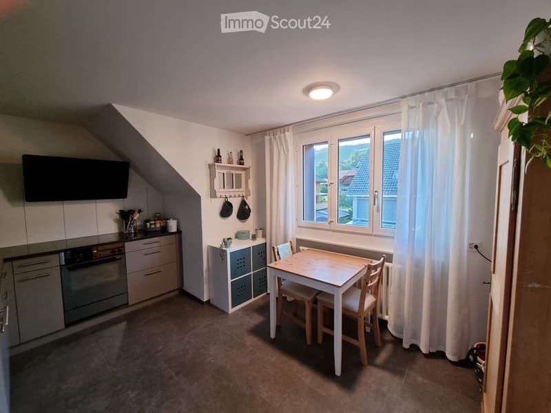 A cozy kitchen and dining area with a small table and chairs, a modern oven, and a window with white curtains.