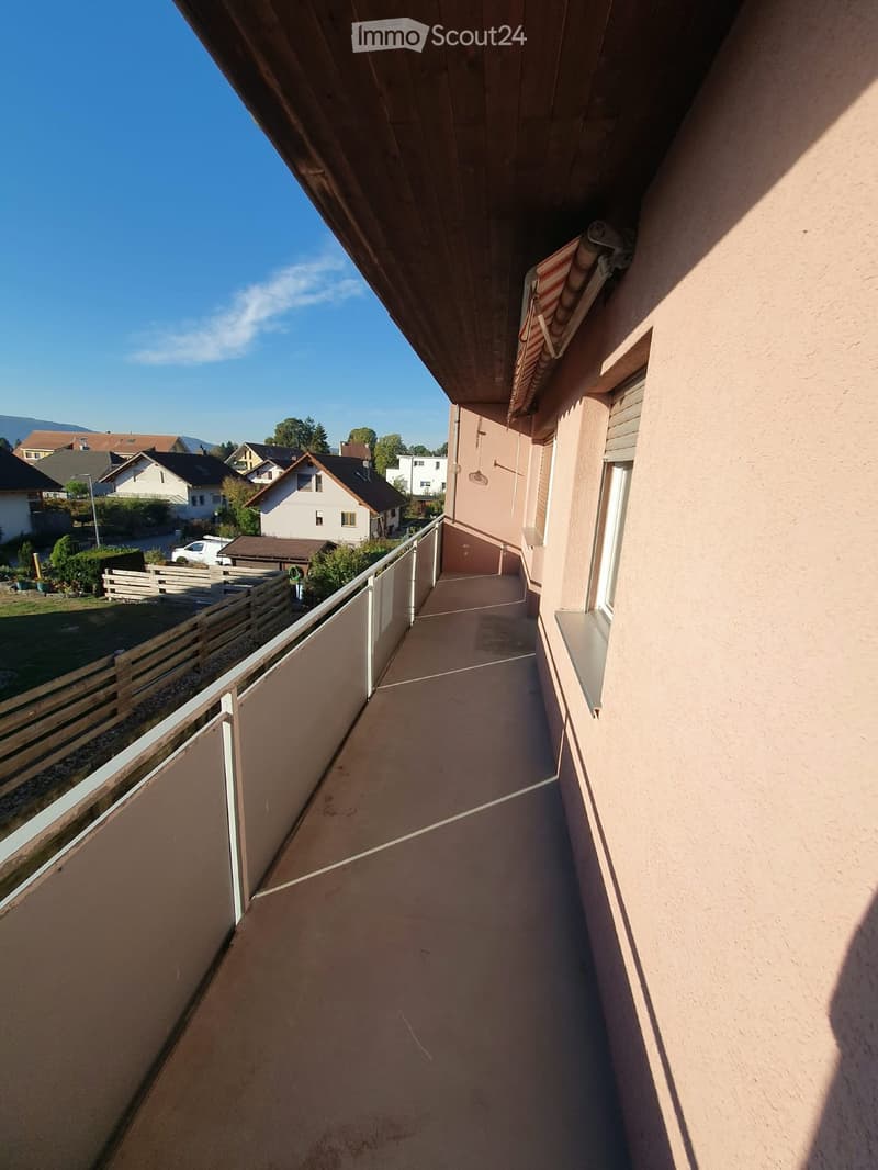 Balcony with a smooth concrete floor, white metal railing, and a view of a residential area with houses and greenery.