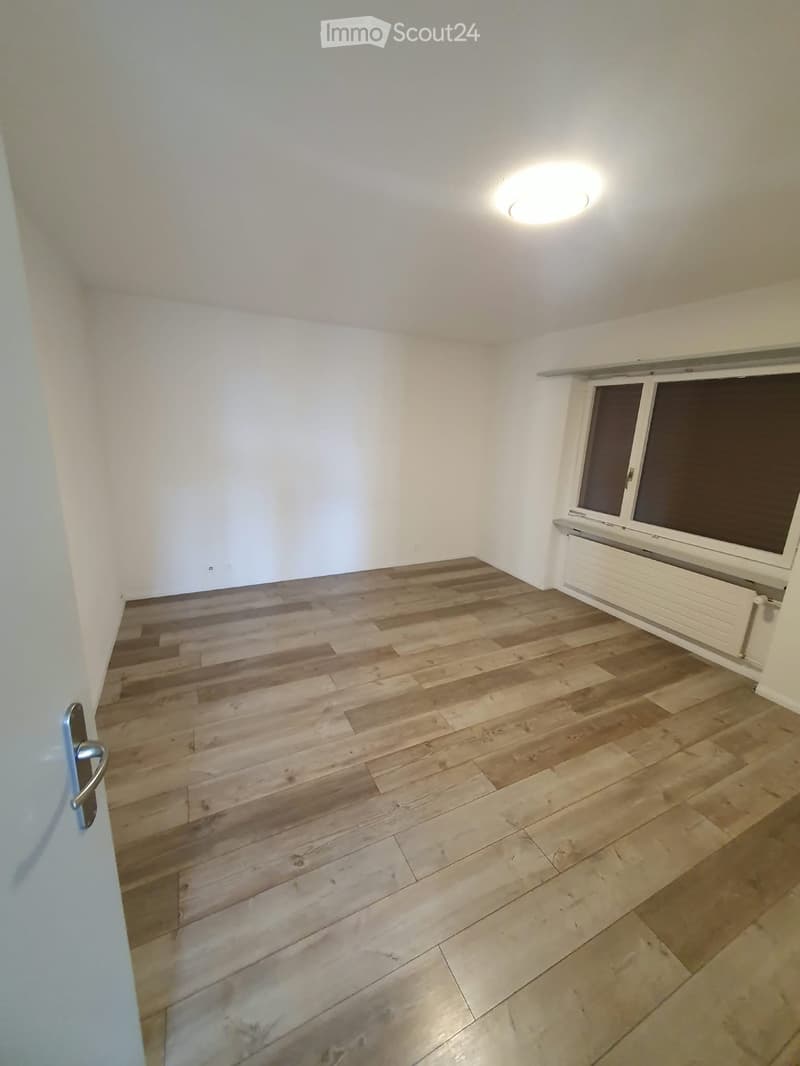 Empty room with wooden flooring, white walls, a window with blinds, and a radiator. No furniture or personal items are present.