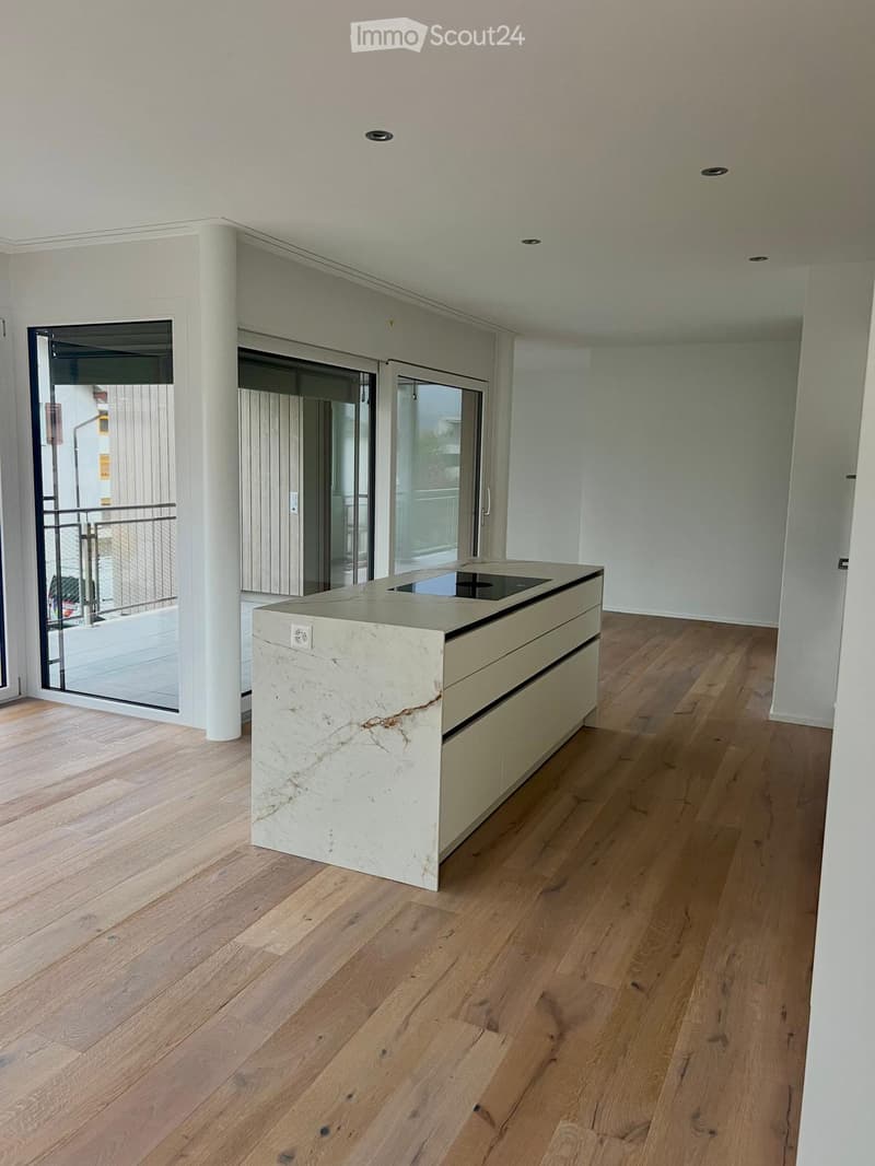 Modern kitchen with a white marble island, wooden flooring, and large glass doors leading to a balcony.