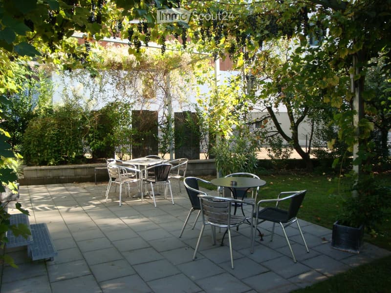 Outdoor seating area with two tables and chairs, surrounded by greenery and grapevines.