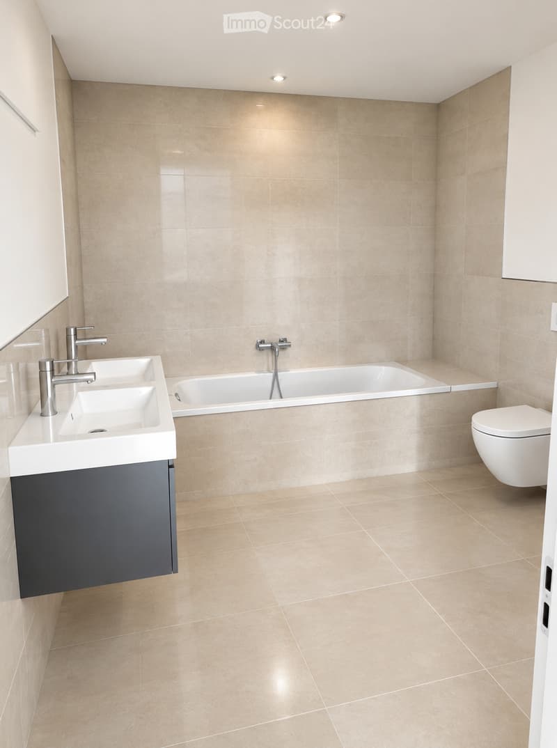 Modern bathroom with beige tiles, double sink, bathtub, toilet, and sleek chrome fixtures.