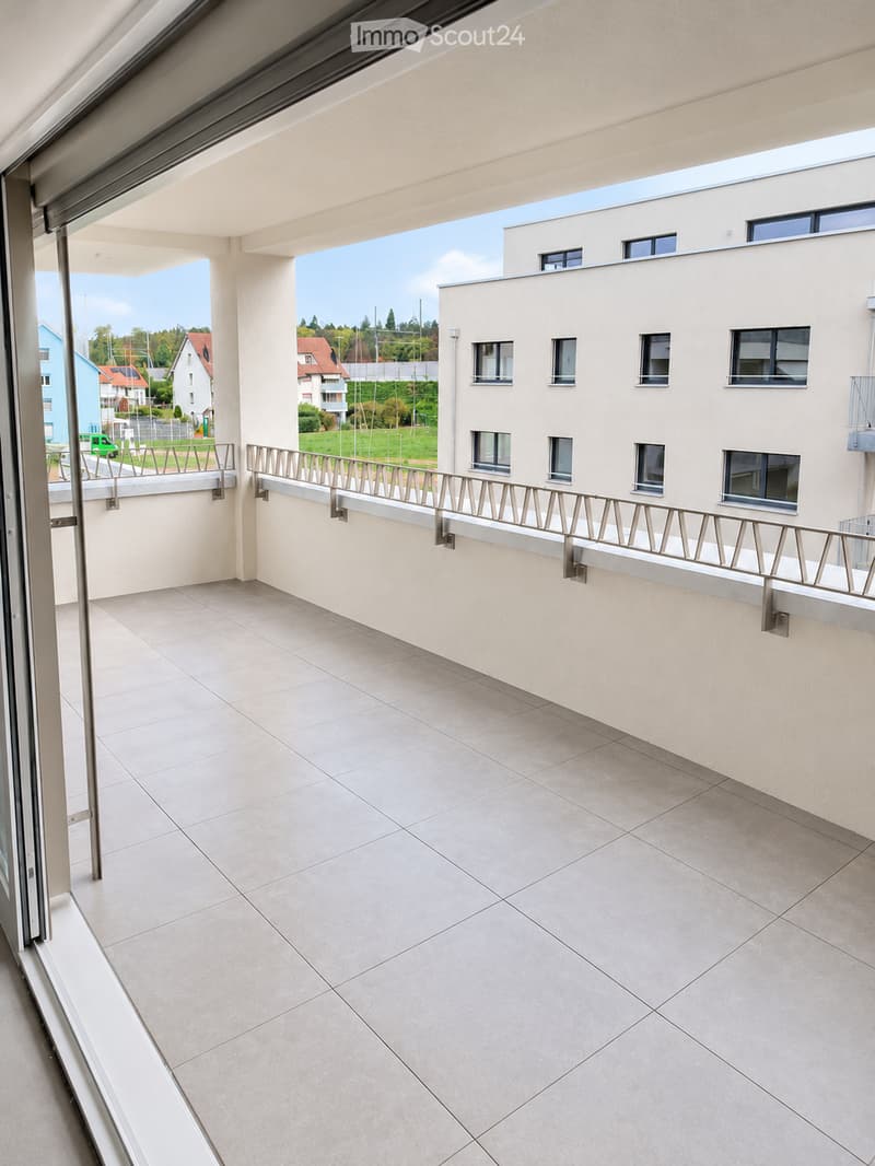 Balcony with tiled floor, metal railing, and a view of a residential area with buildings and greenery.