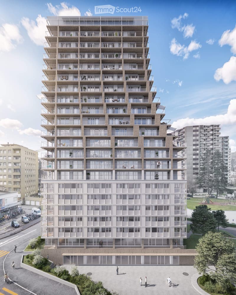 A modern multi-story residential building with numerous balconies and large windows, surrounded by greenery and a paved area.