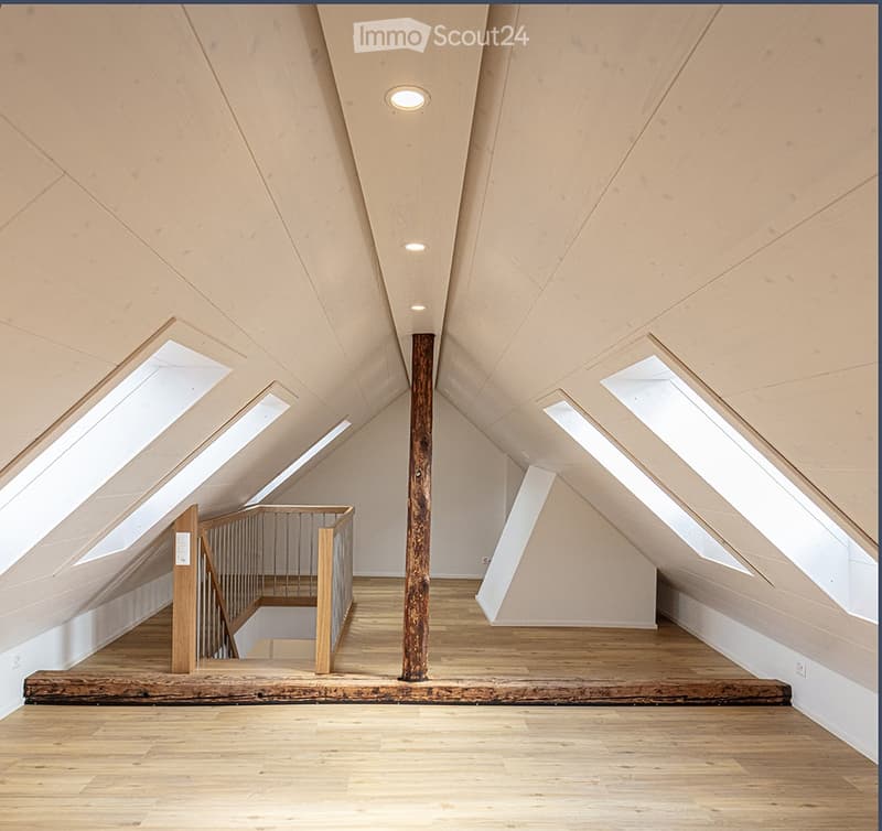 Empty attic space with wooden floors, exposed wooden beams, skylights, and a staircase leading downwards.