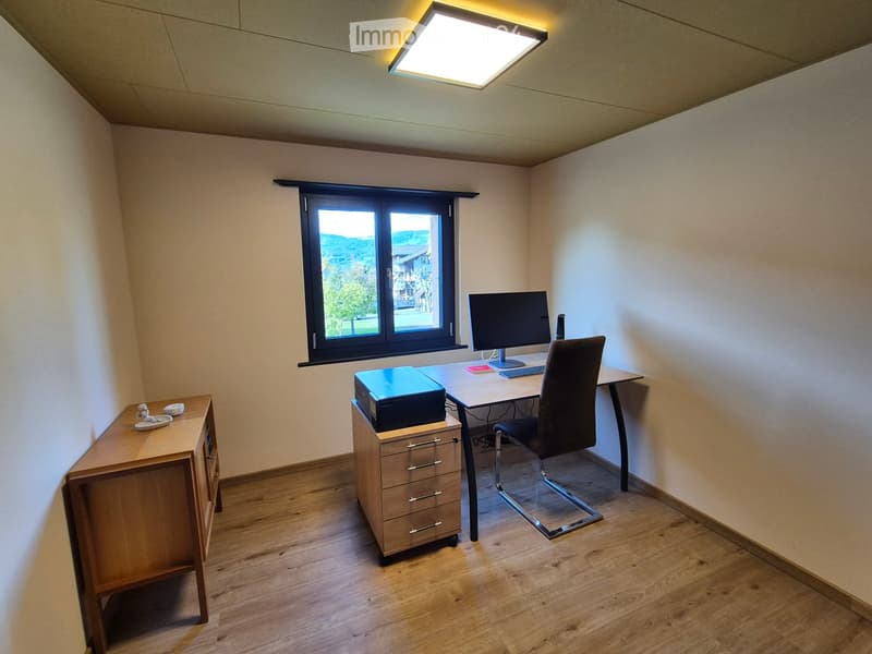 A well-lit, modern office space with a wooden floor, large window, desk, chair, computer, printer, and small cabinet.