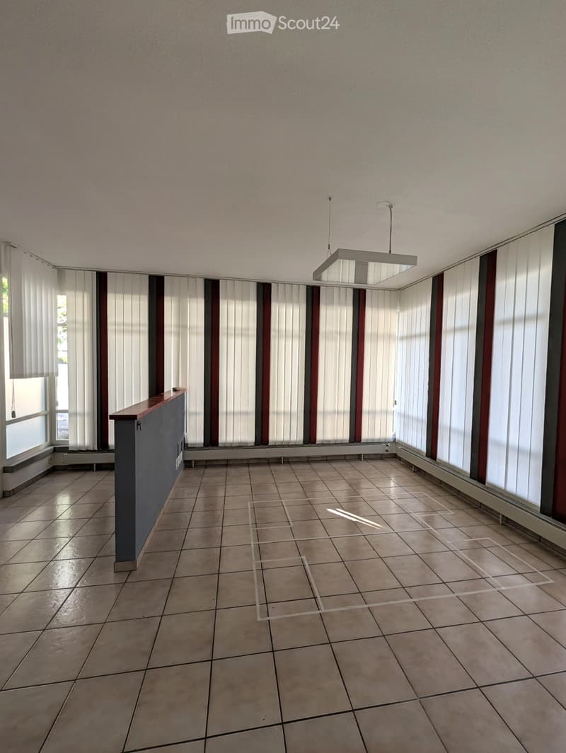 Empty room with tiled floor, white walls, large windows with blinds, and a pendant light fixture.