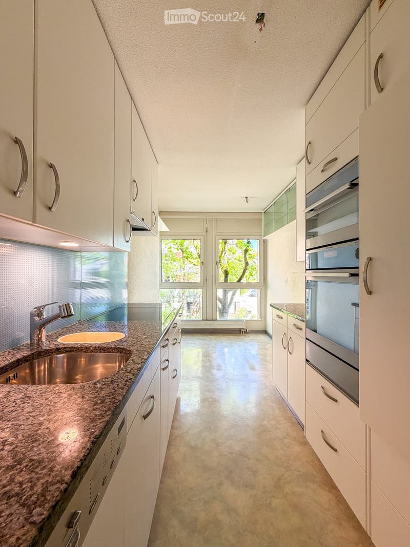 Modern kitchen with granite countertops, stainless steel sink, built-in oven, and white cabinets.