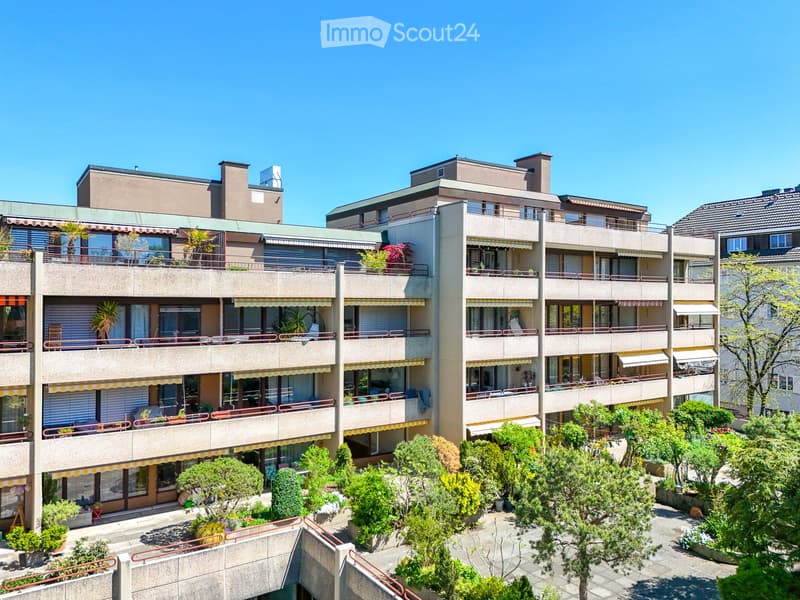 Multi-story residential building with balconies, greenery, and modern architecture.