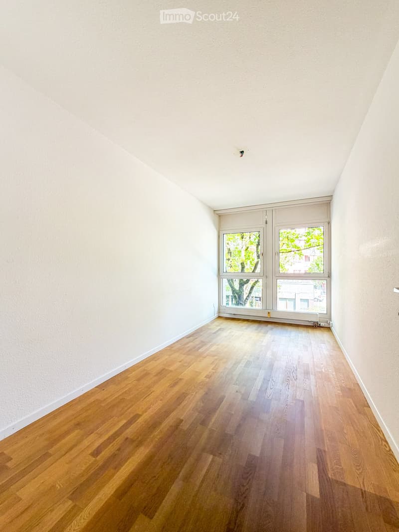 Empty room with wooden flooring and large windows, featuring white walls and a simple, clean design.