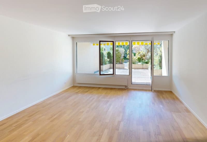 Empty room with light wooden flooring, white walls, large windows, and a sliding glass door leading to an outdoor area.