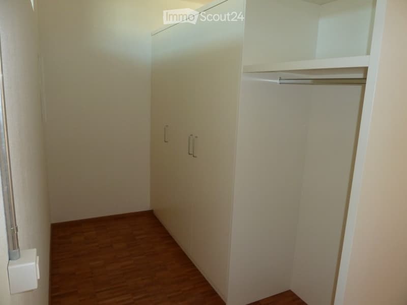 Empty room with wooden floor, white walls, large wardrobe with double doors and hanging rail