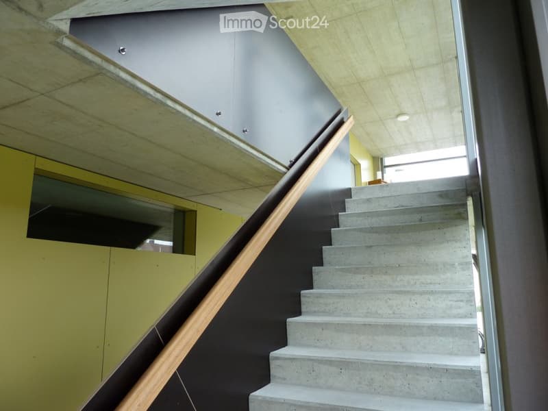 Concrete staircase with a wooden handrail, yellow wall with an openable window, grey ceiling