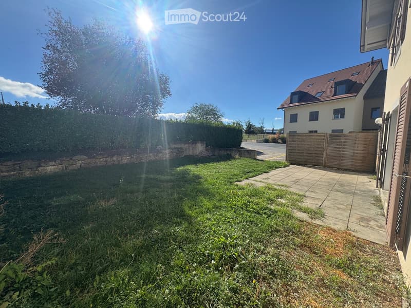 Well-maintained garden with a stone wall, neatly trimmed hedges, and a paved pathway leading to a wooden gate and house entrance.