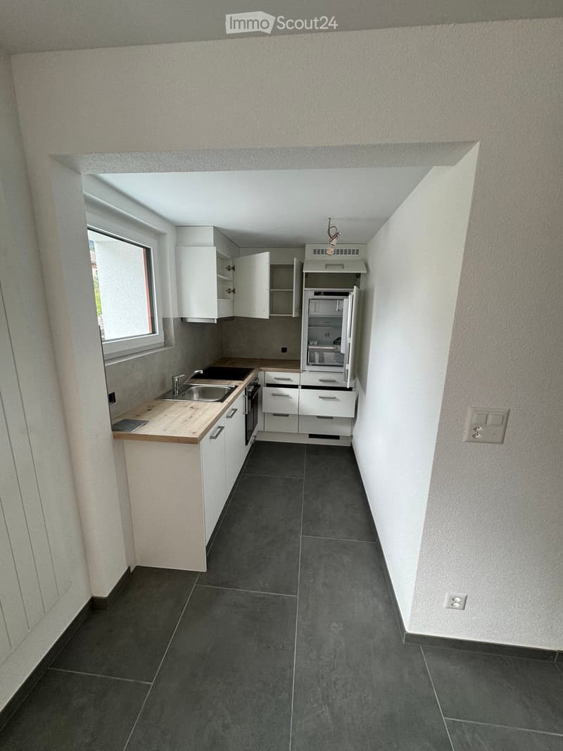 Modern kitchen with white cabinets, dark tiled floor, wooden countertop, stainless steel sink, and built-in refrigerator.