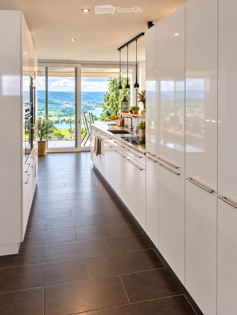 Modern kitchen with white cabinets, dark tiled floor, large windows offering scenic view, sink, faucet, and decorative items.