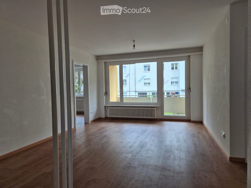 Empty room with large glass doors, white walls, white heater, wooden floor, door to another room