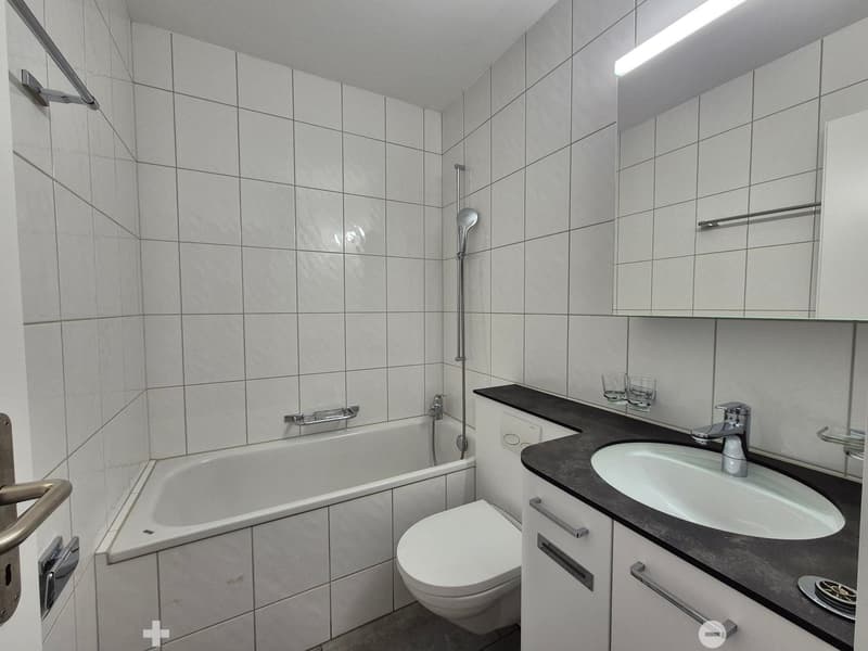 white tiled walls, bathtub, toilet, sink, shower head, white cabinets, countertop, vanity mirror