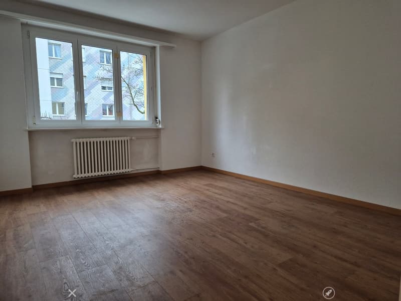 large empty room, wooden floor, white walls, windows, white radiator