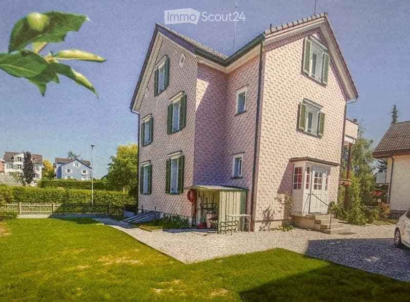 Two-story house with pink and beige exterior, multiple windows, and a small garden area with a table and chairs.