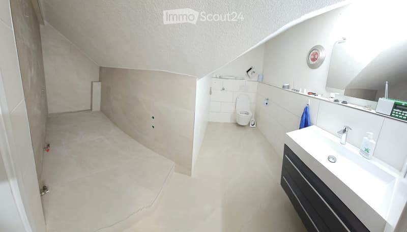 Modern bathroom with white tiles, a sink, toilet, mirror, and a clock on the wall. The space features a sleek design with a dark-colored cabinet under the sink.