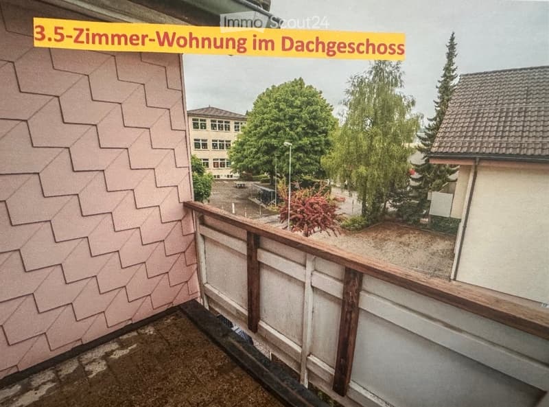 Balcony with wooden railing, tiled floor, and view of surrounding greenery and buildings.