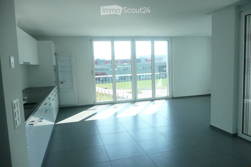 Empty kitchen with white cabinets, black countertops, and a large sliding glass door leading to a balcony.