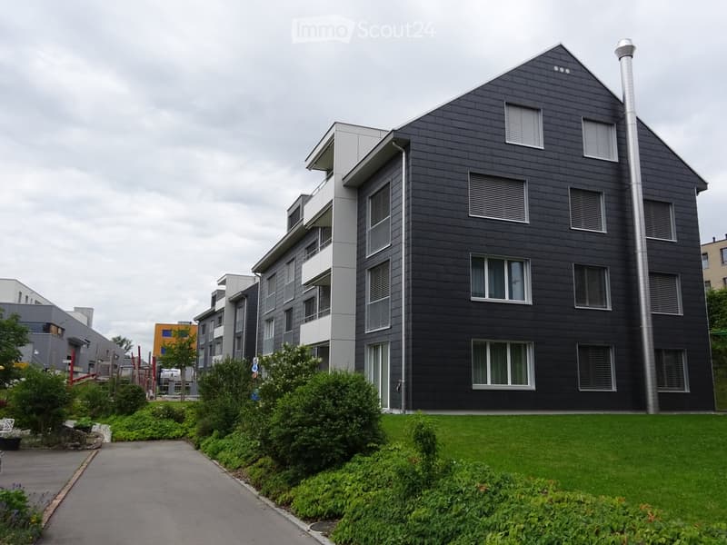Modern apartment building with black exterior, multiple windows, and a green lawn in front.