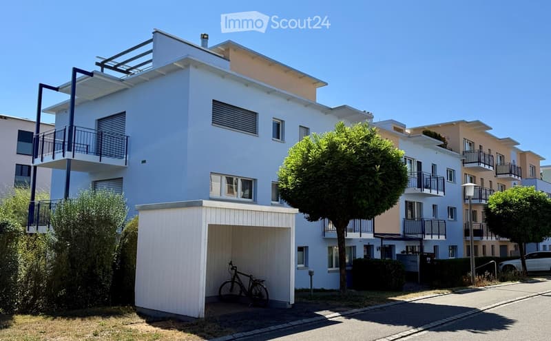Modern two-story apartment building with white exterior, balconies, and a garage with a bicycle inside.