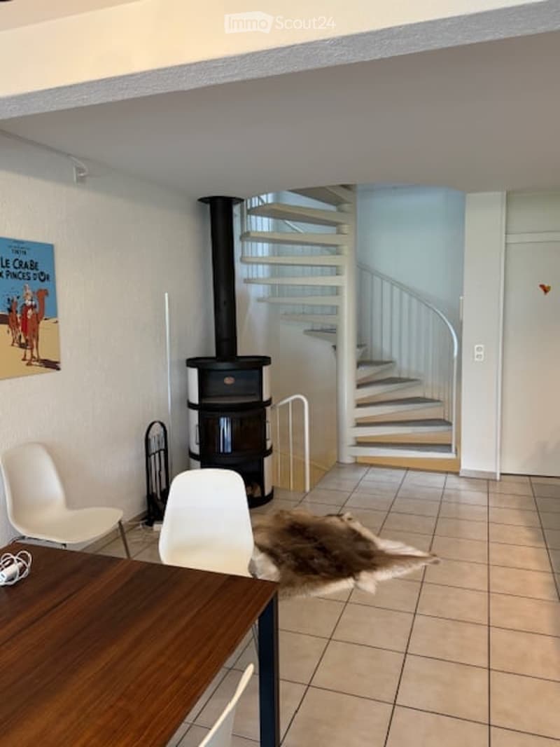 Modern living space with a central fireplace, staircase leading to an upper level, and a wooden table with white chairs.