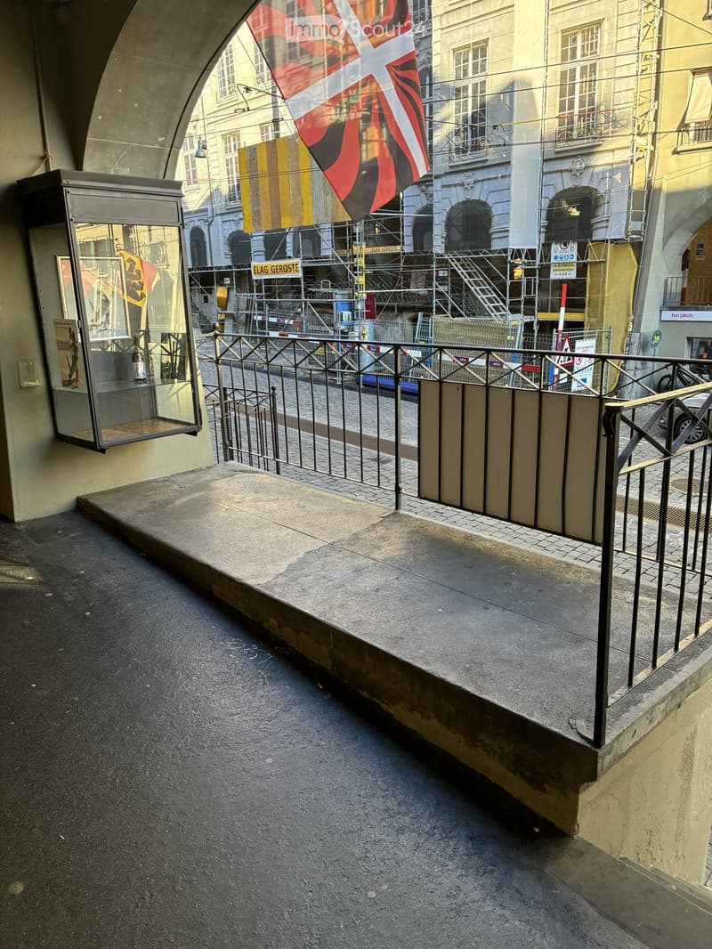 Balcony with metal railing, concrete floor, and a view of a city street with buildings and scaffolding.