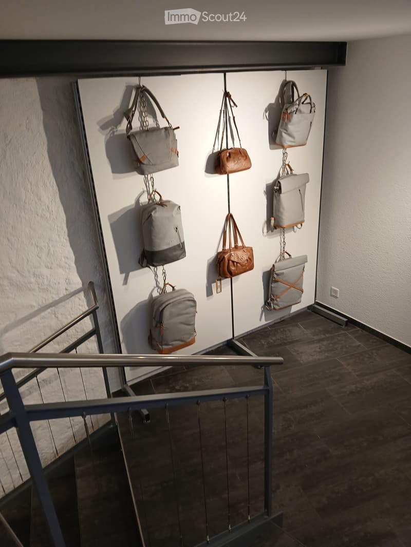 Hallway with a staircase and several bags hanging on the wall, including backpacks and handbags in various colors and styles.