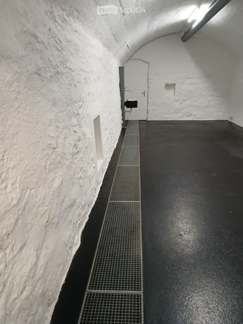 Empty corridor with white stone walls, black floor, and a metal grate along one side.