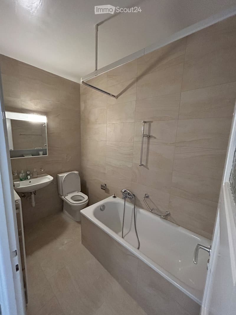 Modern bathroom with beige tiles, bathtub, toilet, sink, and mirror.
