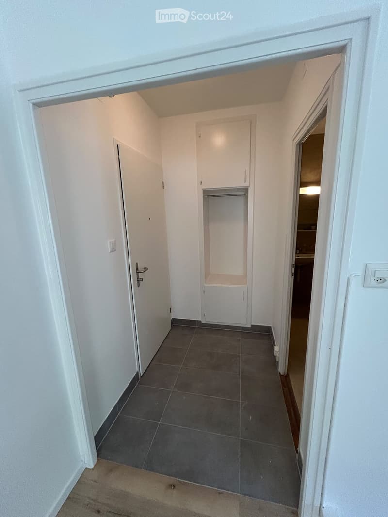 Empty hallway with tiled floor, white walls, and a small closet with a shelf and cabinet. Doors lead to other rooms.