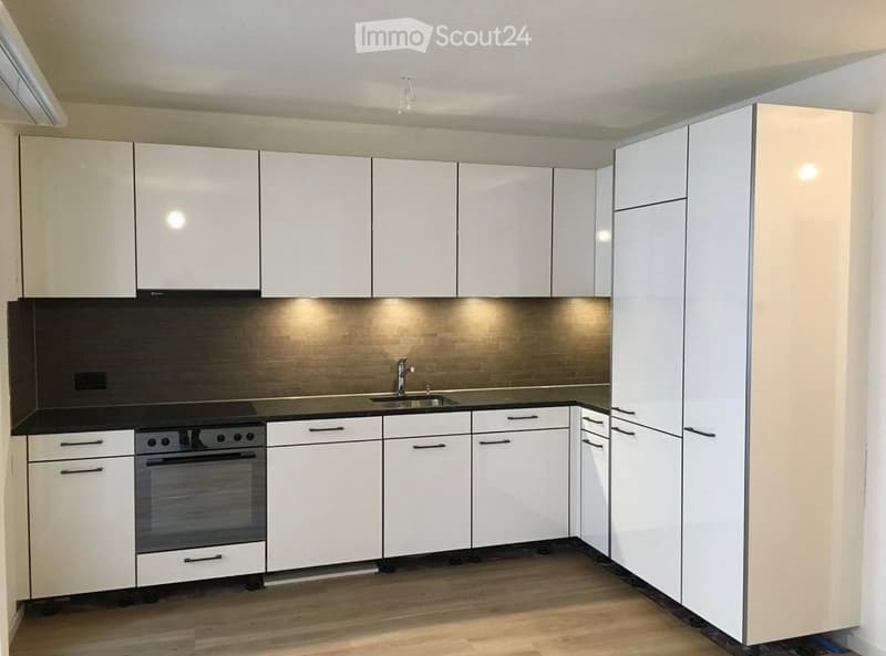 Modern kitchen with white cabinets, black countertops, and a stainless steel sink and oven.