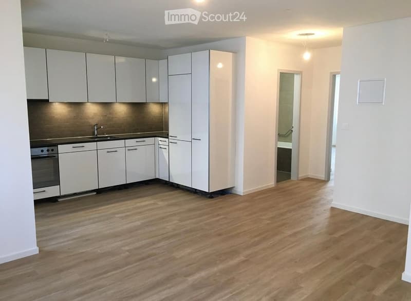 Modern kitchen with white cabinets, stainless steel sink, and oven. Light wooden flooring and bright lighting.