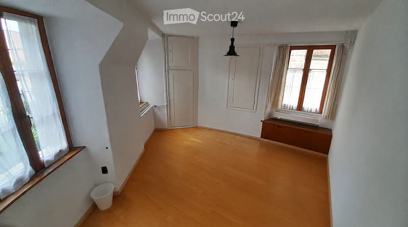 Empty room with wooden flooring, white walls, and large windows with curtains. No furniture or equipment present.
