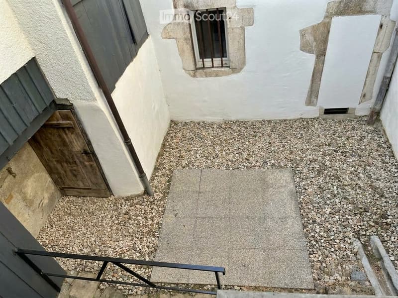 Small raised outdoor area with gravel and concrete steps, adjacent to a building with white walls and a wooden door.