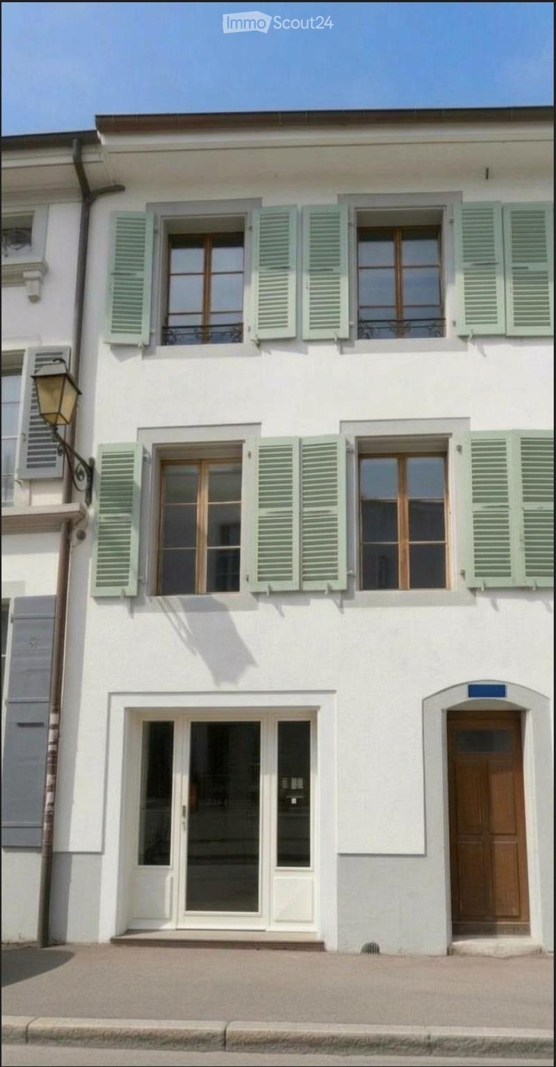 A two-story white building with green shutters, large windows, and a wooden front door.
