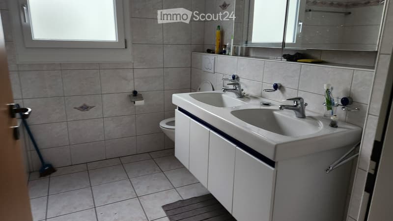 Bathroom with double sink, mirror, toilet, and various toiletries on the counter.