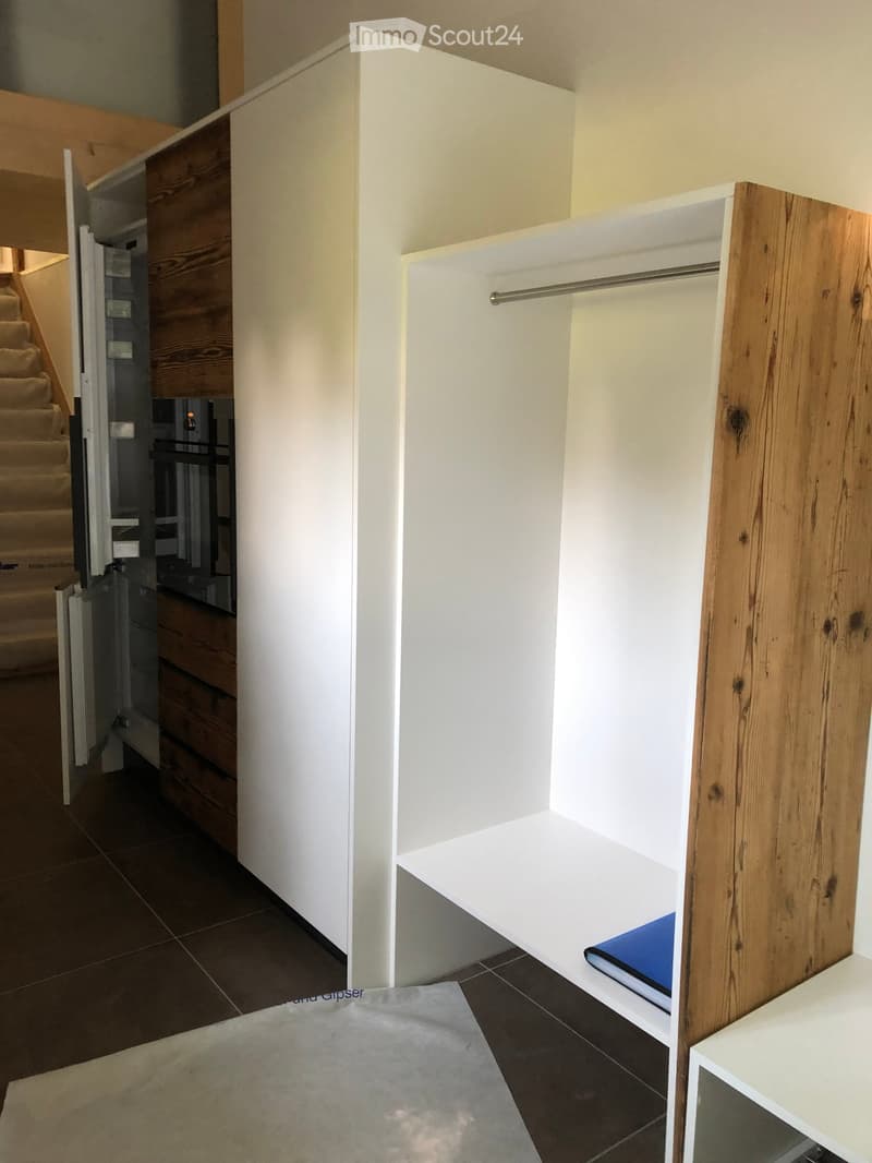Empty room with white built-in closet featuring wooden trim and a hanging rod, adjacent to a staircase with wooden steps and white walls.