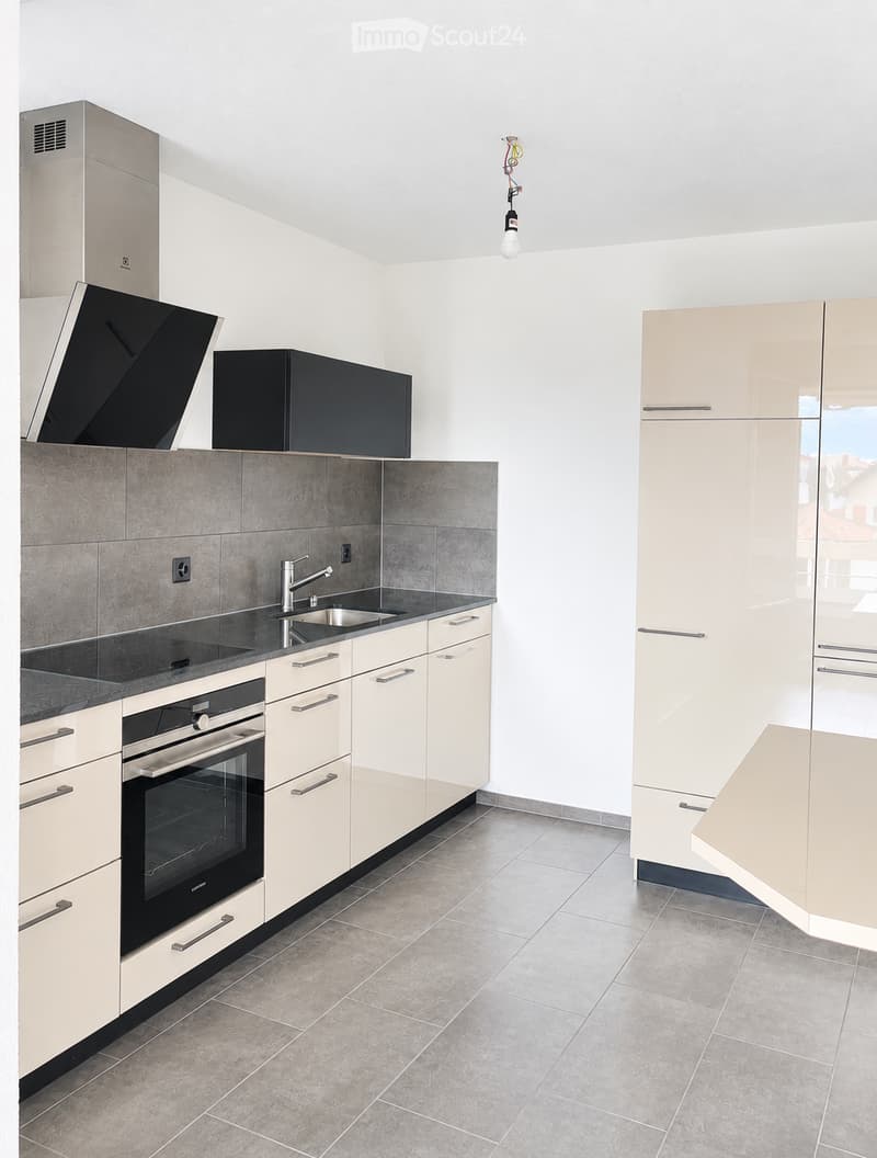 Modern kitchen with light-colored cabinets, stainless steel appliances, and a grey tiled backsplash.