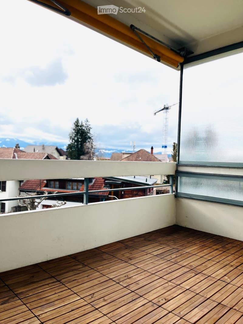 Balcony with wooden decking, white railing, and a view of the surrounding area including houses and mountains.