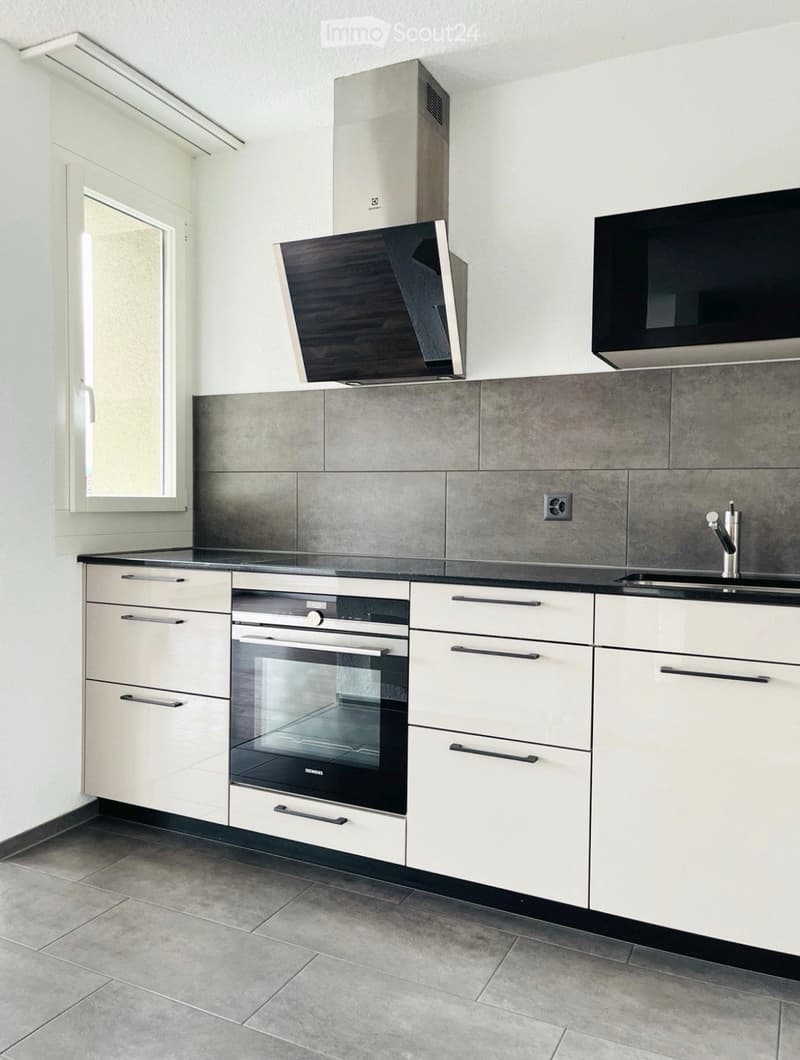 Modern kitchen with white cabinets, stainless steel appliances, and grey tiled backsplash.
