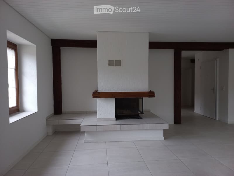 Empty room with a central fireplace, tiled floor, and large window on one side.