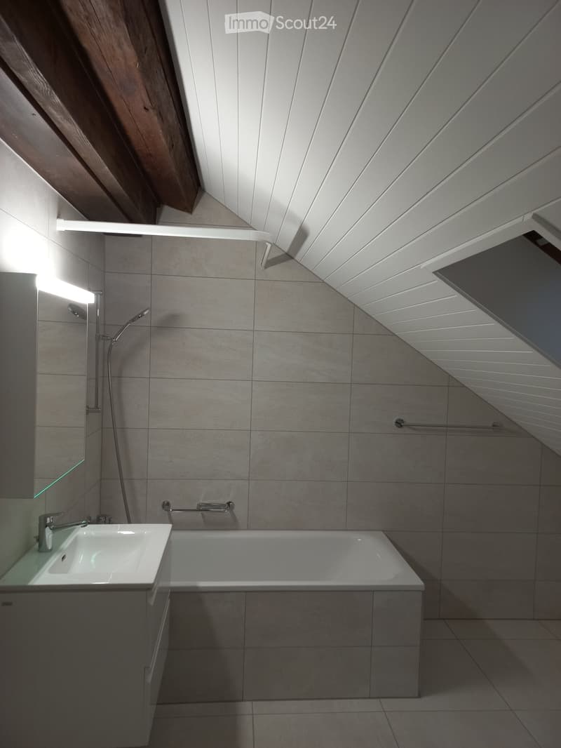 Modern bathroom with a bathtub, sink, and showerhead, featuring grey tiles and a sleek design.