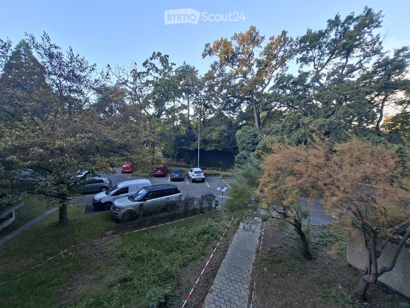 Aerial view of a parking lot surrounded by trees and greenery, with several parked cars and a paved pathway.